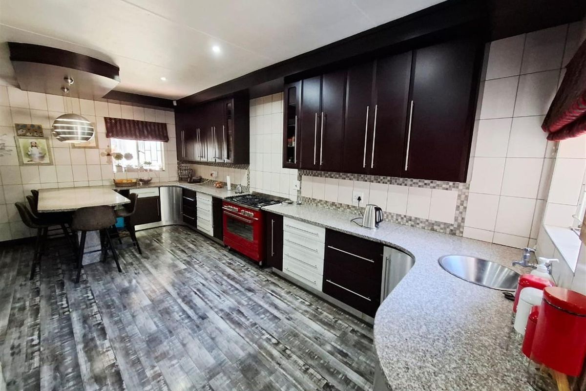 Spacious kitchen featuring dark cabinetry, granite countertops, a distinctive red oven, and modern laminate flooring with an integrated breakfast nook area.