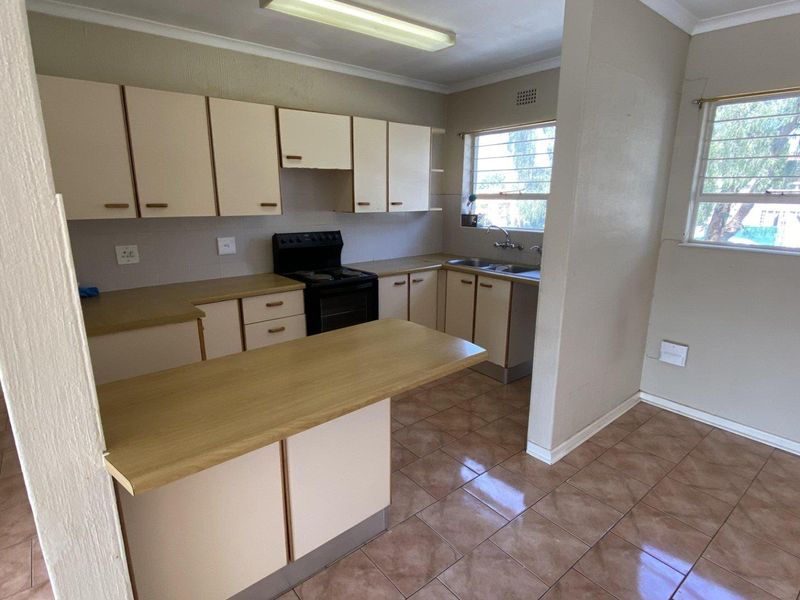 A functional kitchen featuring laminate countertops, built-in cabinetry, a double basin sink, and tiled flooring, offering a clean and practical layout.