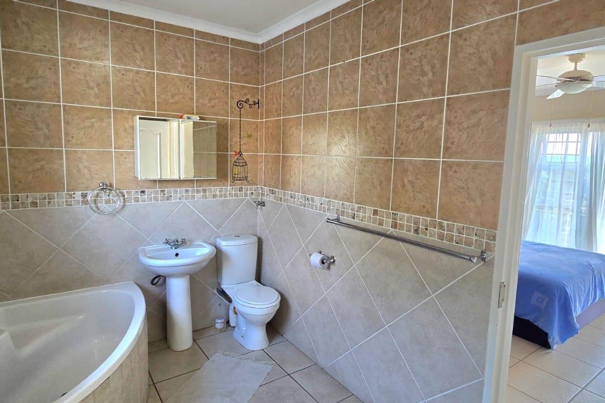 A functional bathroom featuring a corner bathtub, pedestal basin, and toilet with neutral wall tiling and a view into the adjacent bedroom.