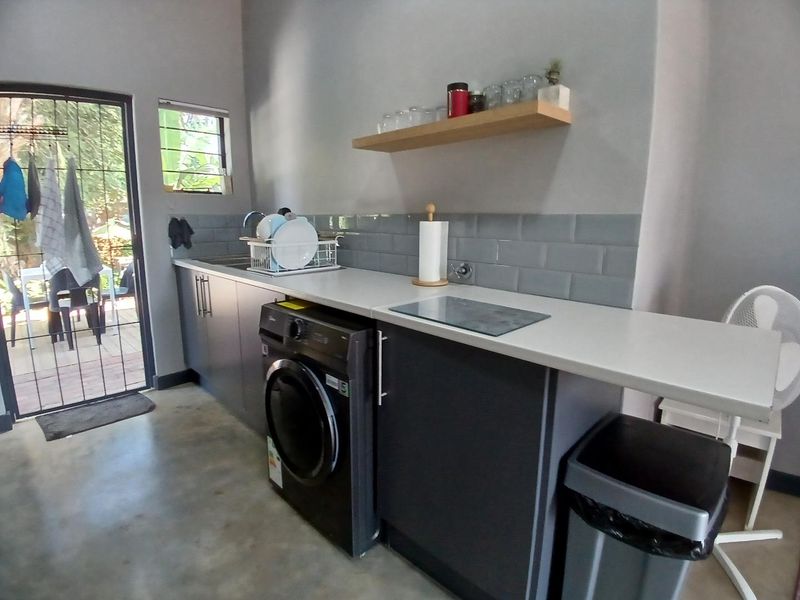 A modern laundry area featuring sleek dark cabinetry, subway tile backsplash, concrete flooring, and direct access to an outdoor patio space.
