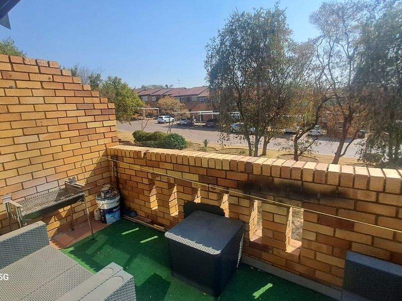 An outdoor balcony featuring a brick balustrade and a built-in braai area, overlooking the complex parking and surrounding trees.