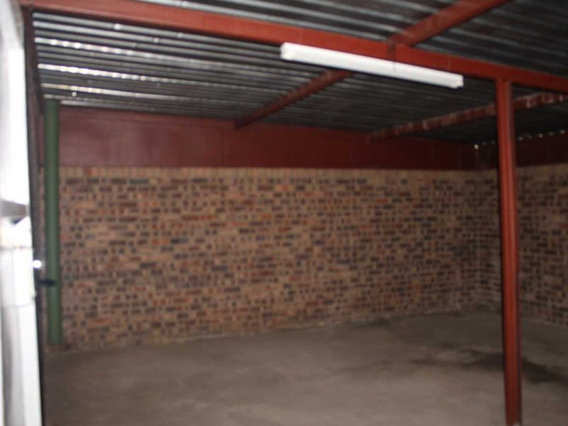 An empty, utilitarian garage space featuring exposed brick walls, a corrugated metal ceiling, and concrete flooring, suitable for storage or workshop use.