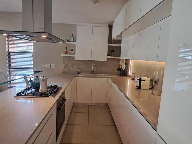 Modern kitchen featuring sleek white gloss cabinetry, stone countertops, integrated gas hob, extractor fan, and built-in oven with tiled flooring.