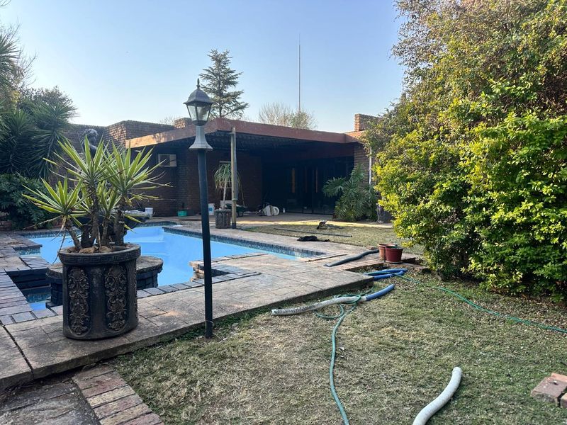 Outdoor pool area featuring a swimming pool, brick paving, and a covered patio space set within a garden environment.
