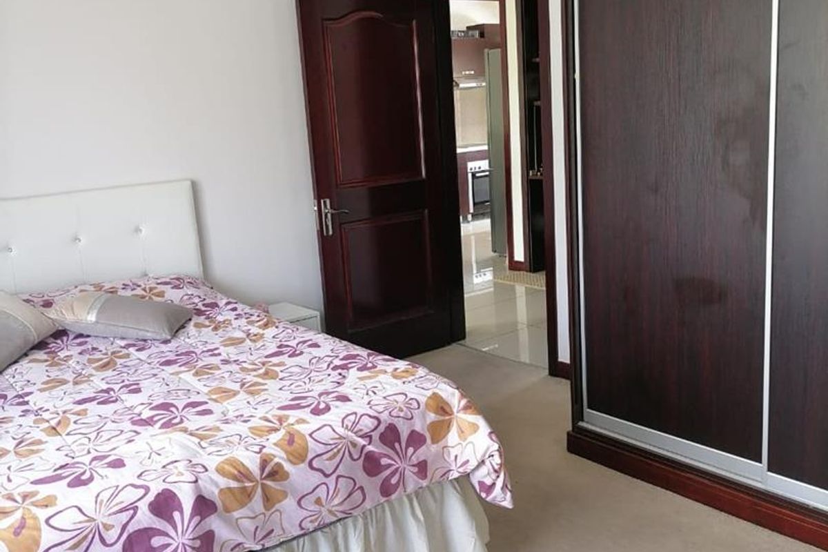 A bedroom featuring neutral carpeting, dark wood built-in sliding door wardrobes, and a doorway leading to an adjacent living area.