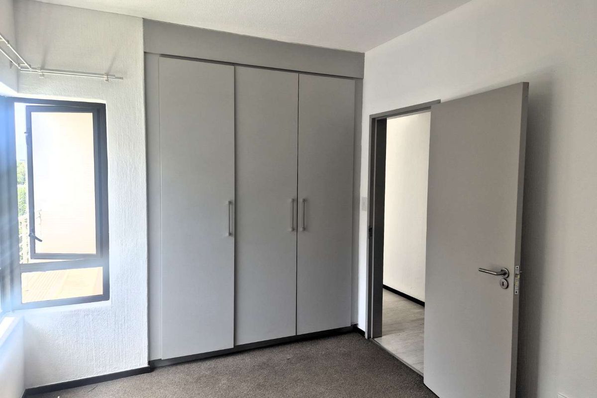 A clean, empty bedroom featuring neutral grey built-in cupboards, carpeted flooring, and a modern casement window, offering a blank canvas for personalization.
