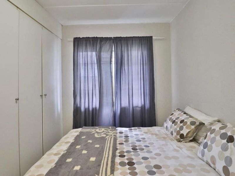 A functional bedroom featuring built-in cupboards and a window with curtaining, offering a neutral space ready for personalization.