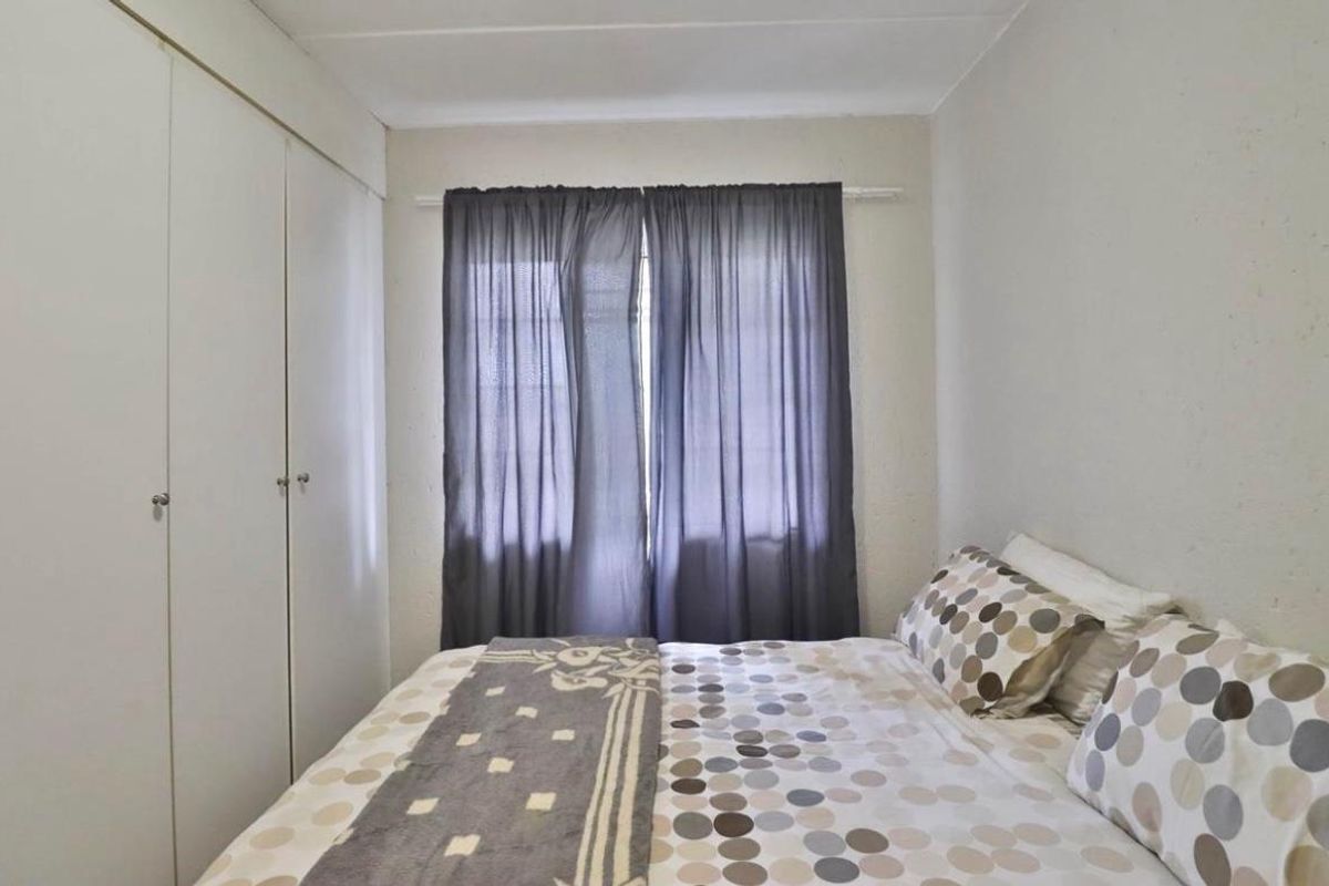 A functional bedroom featuring built-in cupboards and a window with curtaining, offering a neutral space ready for personalization.