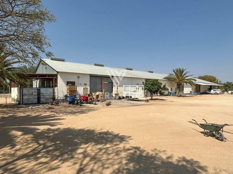 Exterior view of a large industrial warehouse facility featuring corrugated metal roofing and sliding access doors on a spacious gravel yard.