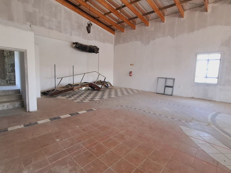 An expansive, unfinished open-plan commercial space featuring exposed timber roof trusses, tiled flooring, and large windows, offering a blank canvas for renovation.