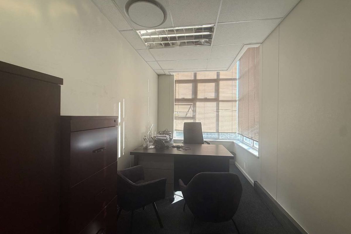 A functional office space featuring a suspended ceiling with recessed lighting, carpeted flooring, and large corner windows with venetian blinds for natural light control.