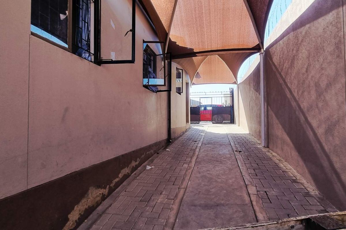 A paved side passage featuring a shade sail covering, providing a sheltered walkway along the side of the property.