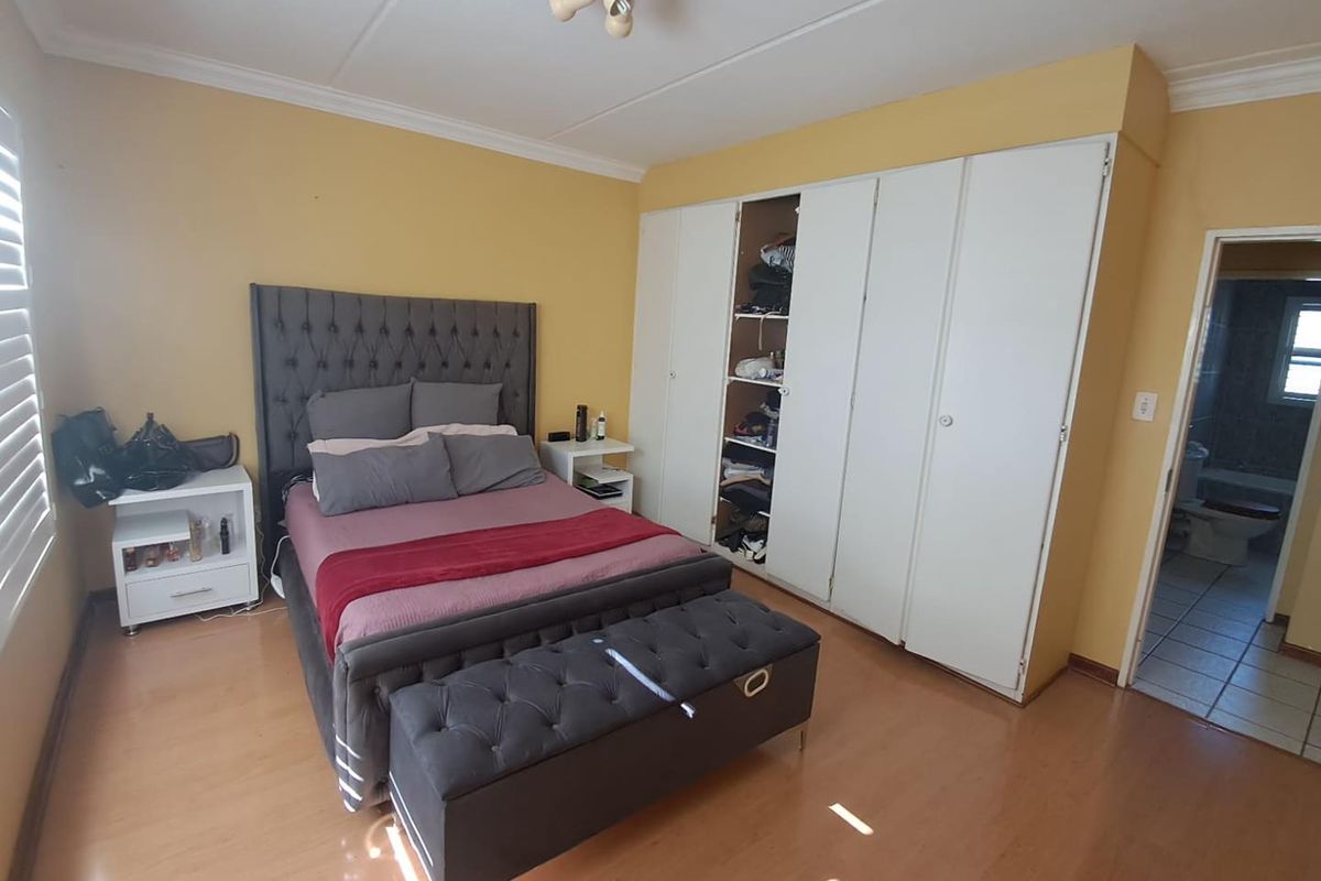 Spacious bedroom featuring built-in cupboards, laminate flooring, and neutral wall tones, offering a functional layout with direct access to an en-suite bathroom.