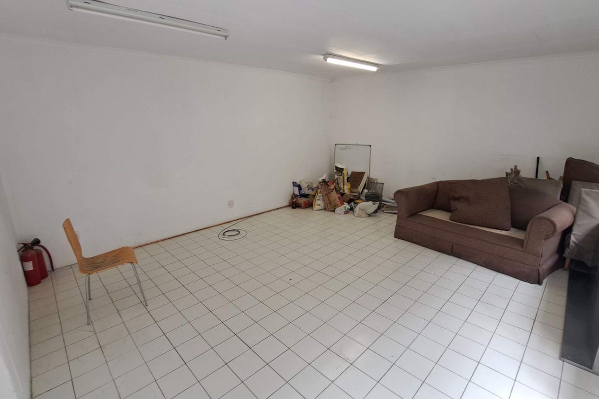 A basic living area featuring white walls, ceramic tiled flooring, and fluorescent strip lighting, currently used as a multi-purpose space.