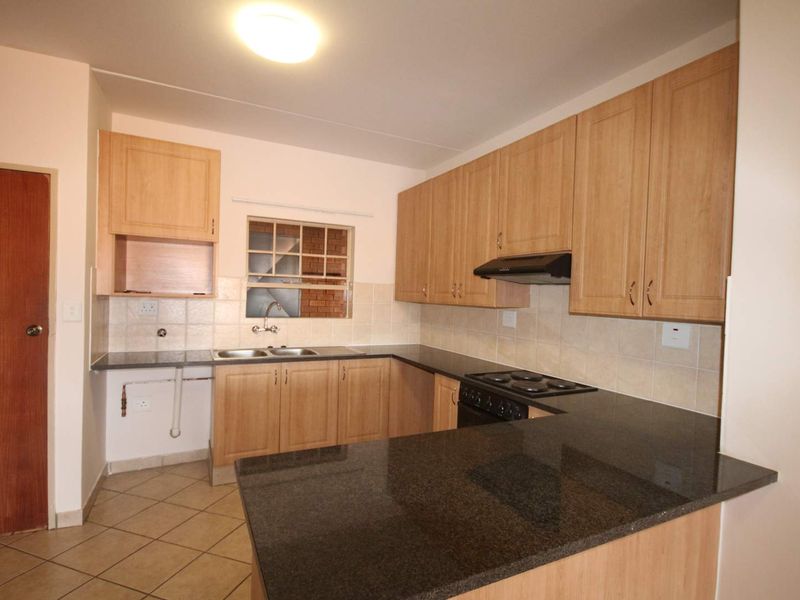 A functional kitchen featuring laminate cabinetry, granite countertops, a double bowl sink, and an integrated electric hob with an extractor fan.