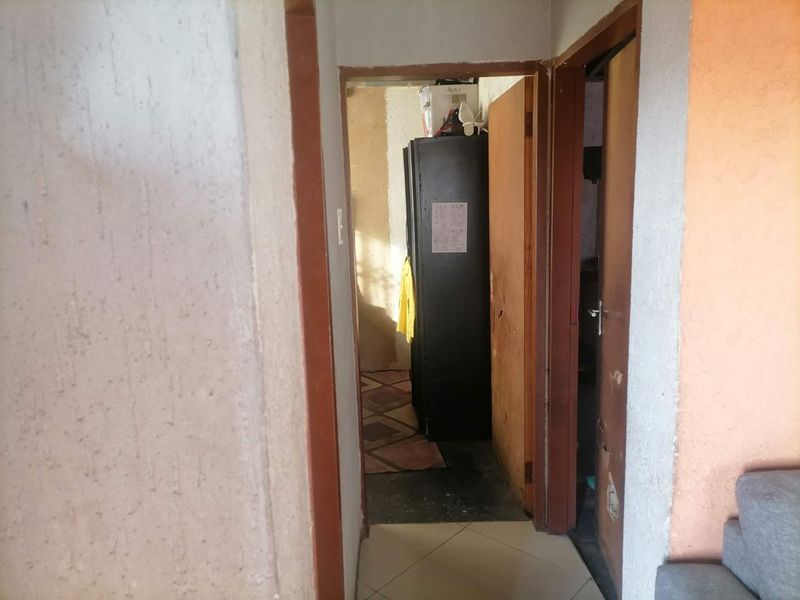A narrow interior hallway featuring tiled flooring and wooden door frames, showing signs of wear on the walls and door surfaces.