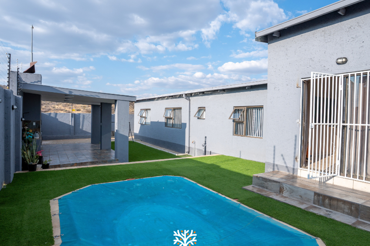 Rear exterior view featuring a swimming pool with cover, artificial lawn, and a covered patio area attached to the main house structure.