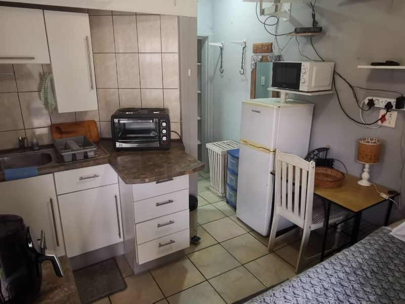 Compact open-plan kitchenette area featuring built-in cabinetry, laminate countertops, and tiled backsplash, integrated within a small living space.