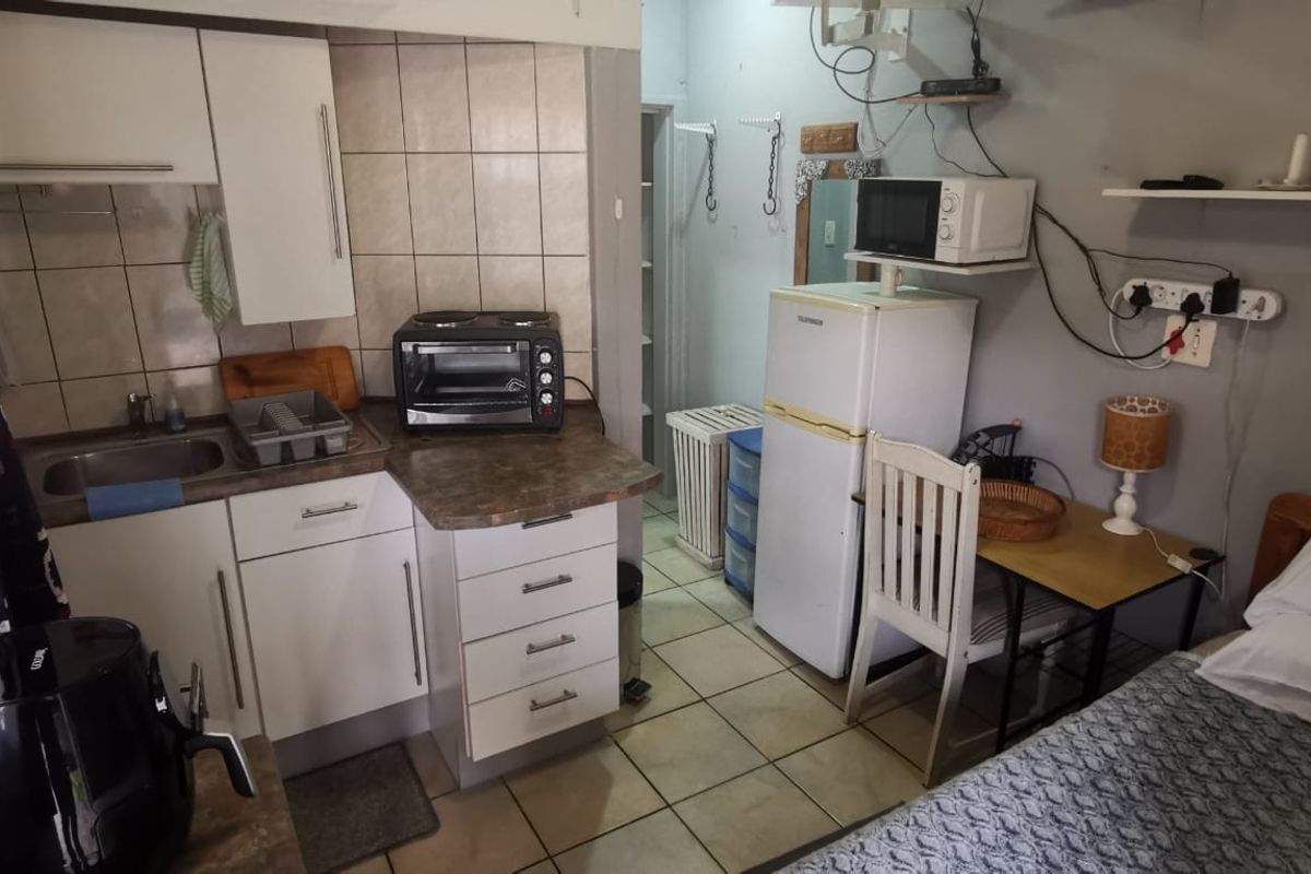 Compact open-plan kitchenette area featuring built-in cabinetry, laminate countertops, and tiled backsplash, integrated within a small living space.