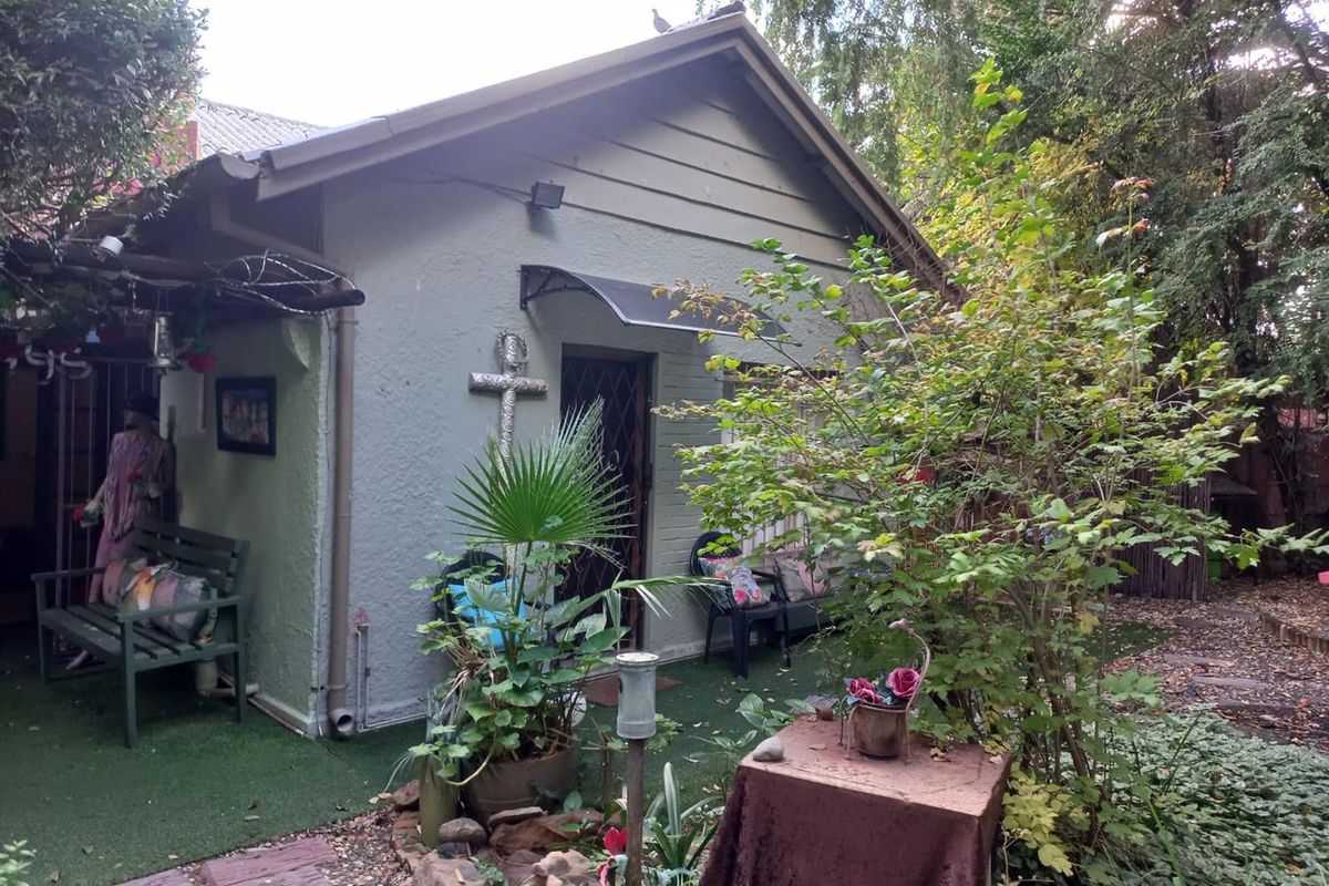 A view of the rear exterior of the house, featuring a covered patio area, landscaped garden, and established trees.