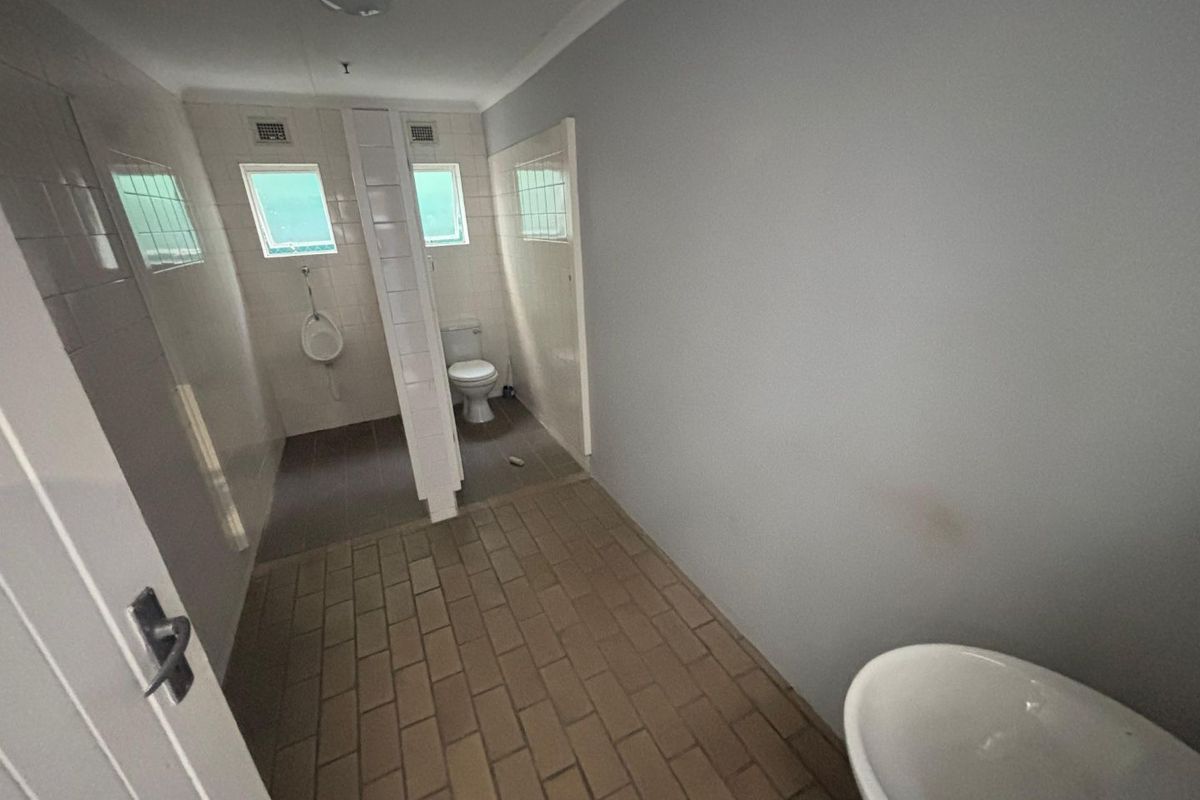 Functional industrial restroom facility featuring tiled flooring, partitioned toilet and urinal stalls, and a wall-mounted basin.
