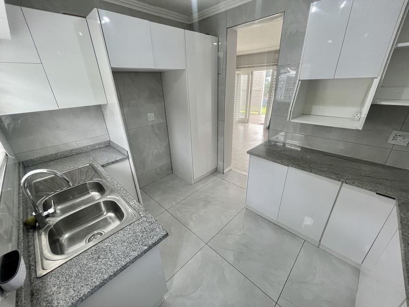 Modern kitchen featuring gloss white cabinetry, granite countertops, a double bowl stainless steel sink, and large format porcelain floor tiles.