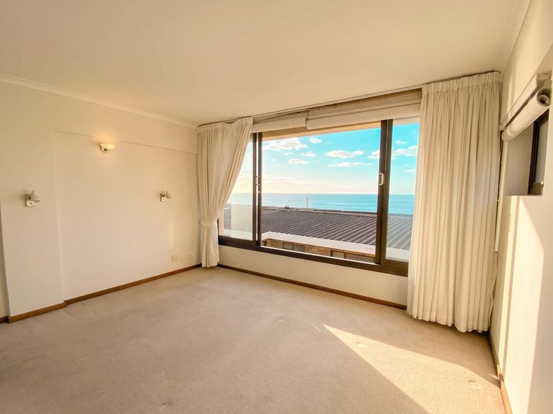 A bright, empty bedroom featuring neutral carpeting and a large window offering expansive ocean views.