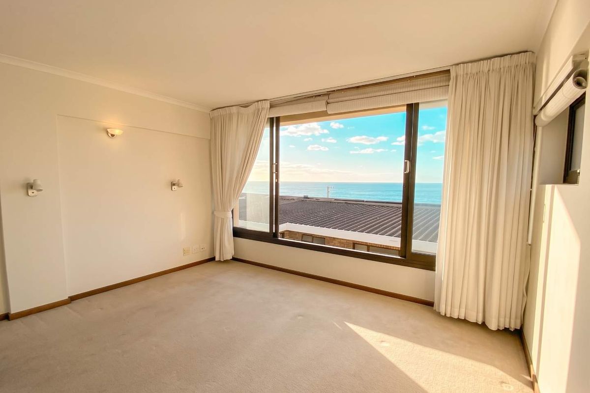 A bright, empty bedroom featuring neutral carpeting and a large window offering expansive ocean views.