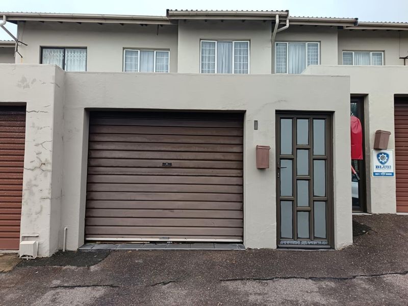 Front elevation of a townhouse featuring a single garage, pedestrian entrance door, and upper-level windows with visible exterior wall cracking.