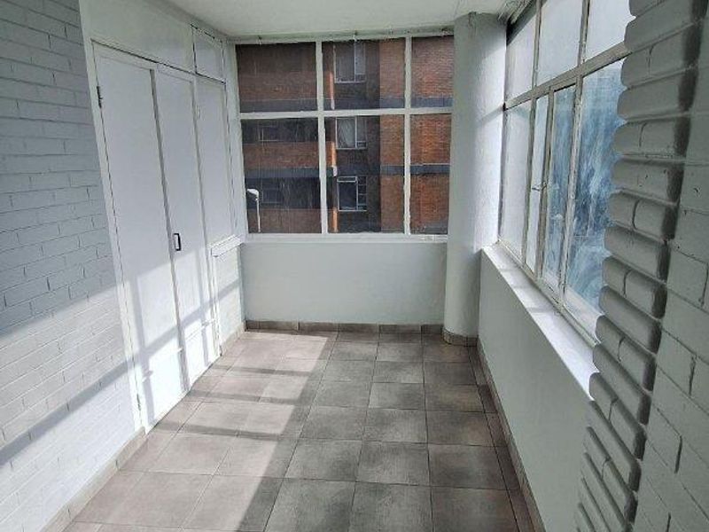 A bright, enclosed balcony featuring tiled flooring, large windows, and a built-in storage cupboard, offering a versatile space for relaxation or additional storage.