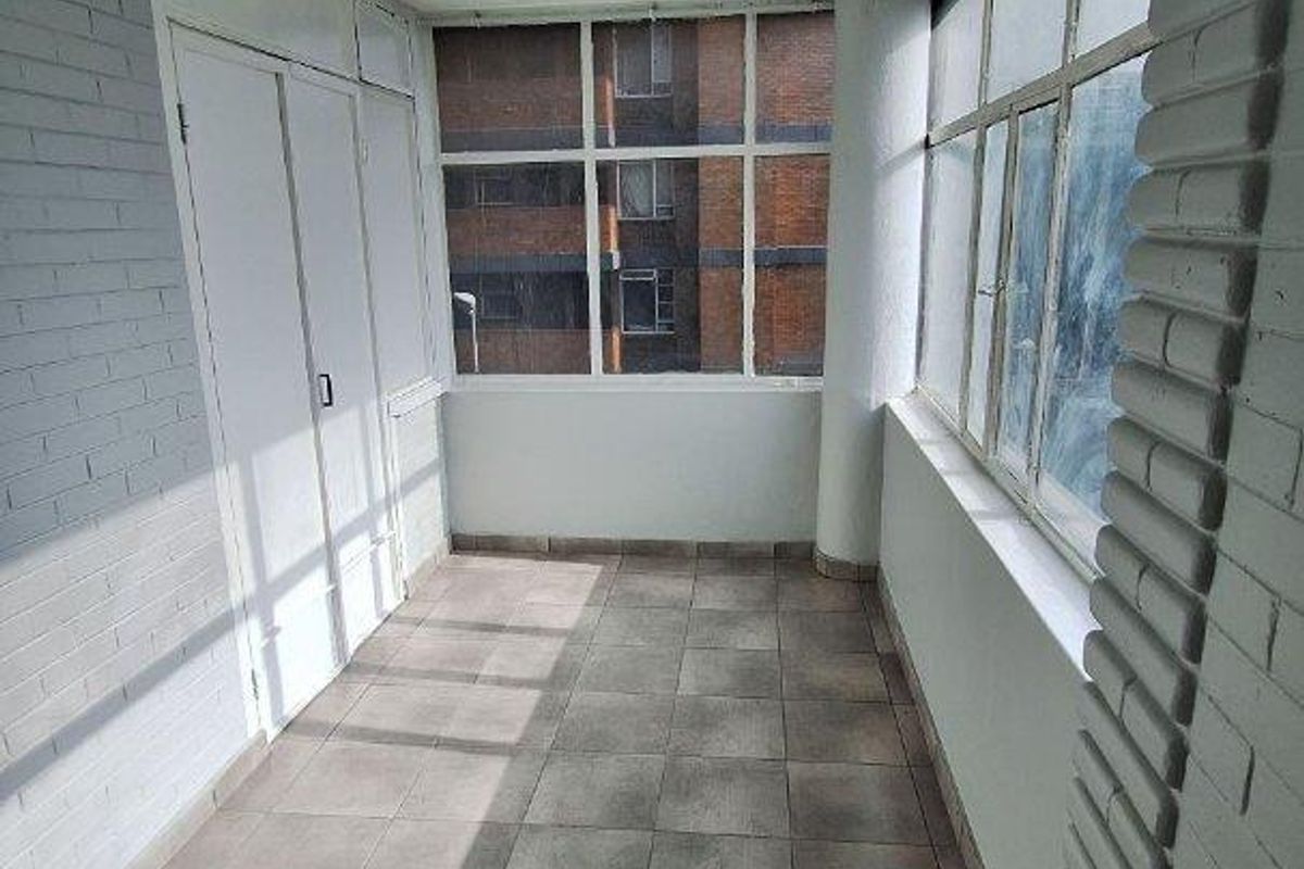 A bright, enclosed balcony featuring tiled flooring, large windows, and a built-in storage cupboard, offering a versatile space for relaxation or additional storage.