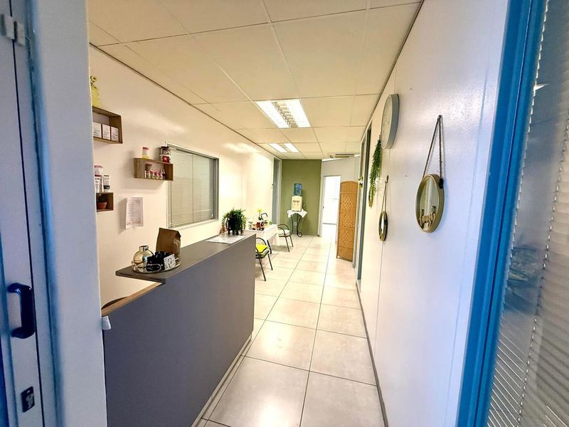 A functional office reception area featuring tiled flooring, a built-in reception desk, and suspended ceiling lighting.