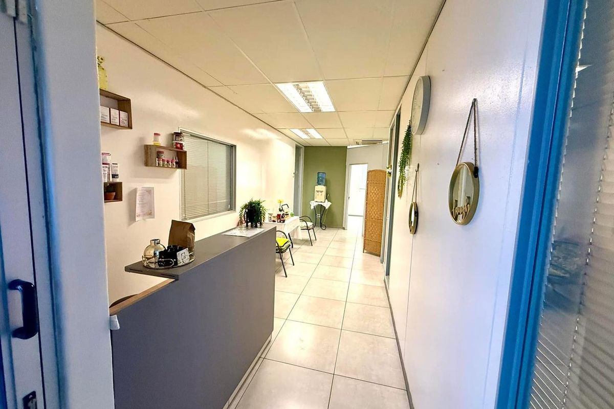 A functional office reception area featuring tiled flooring, a built-in reception desk, and suspended ceiling lighting.
