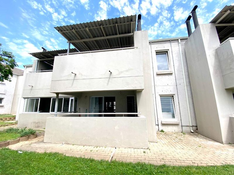 Rear view of the apartment building featuring a ground floor patio, upper balcony with metal roofing, and paved outdoor space.