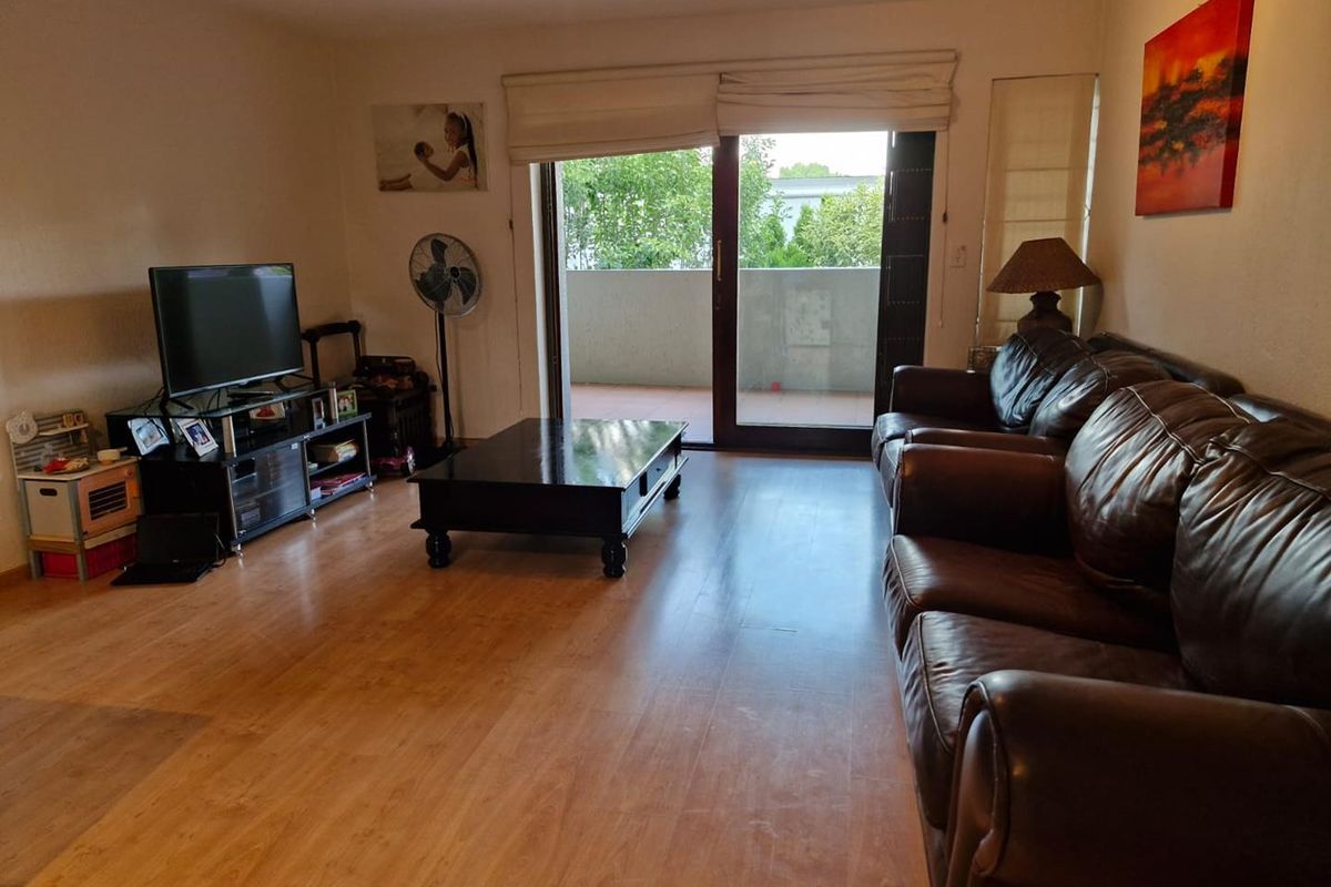 A living room featuring laminate wood flooring and large sliding glass doors that provide access to an outdoor balcony area.