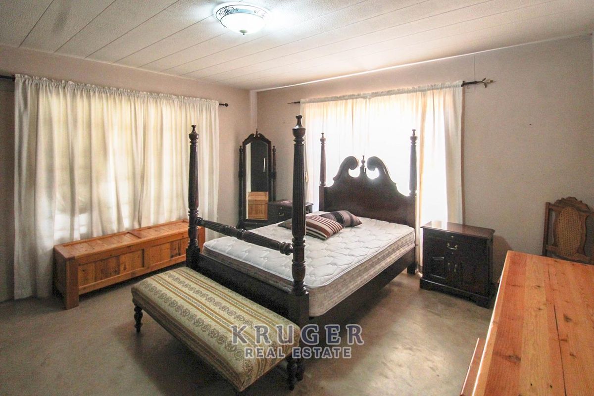A spacious bedroom featuring neutral walls, large windows with curtains, and a central ceiling light fixture.