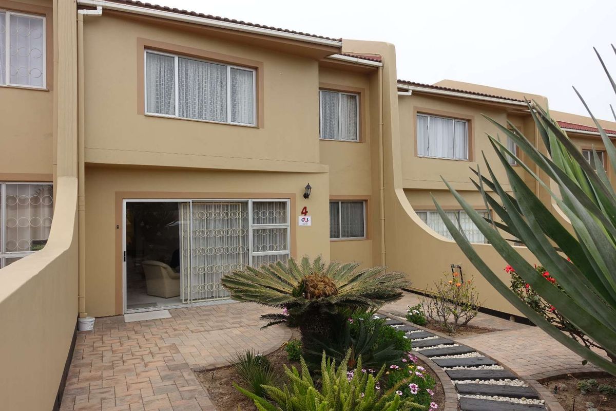 Rear view of a townhouse featuring a paved patio area, sliding glass door access, and established garden landscaping.