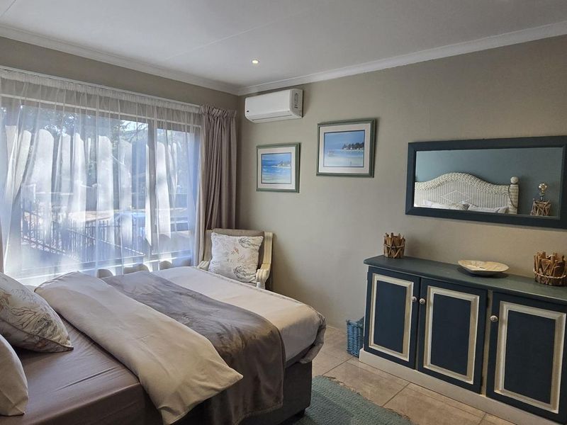 A well-maintained bedroom featuring tiled flooring, a split-system air conditioner, and a large sliding glass door providing natural light.