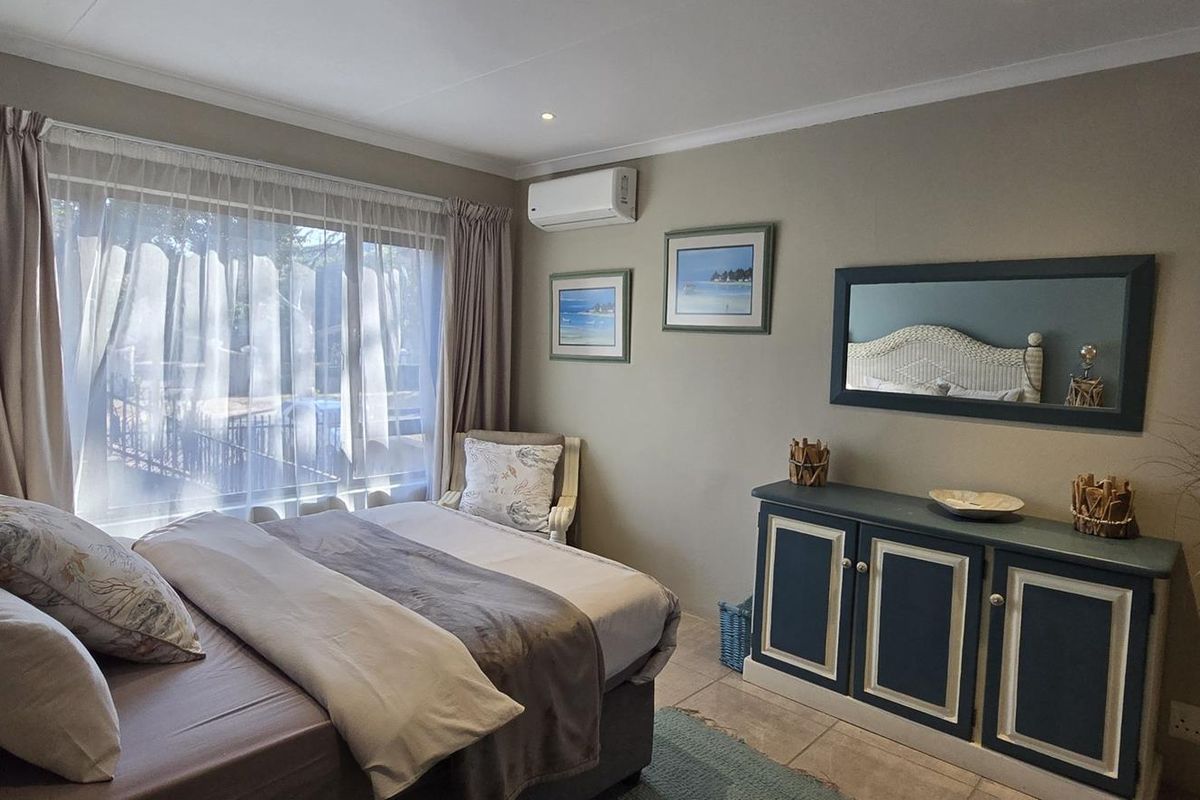 A well-maintained bedroom featuring tiled flooring, a split-system air conditioner, and a large sliding glass door providing natural light.