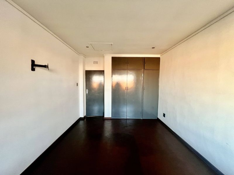 An empty bedroom featuring built-in cupboards, dark flooring, and a wall-mounted TV bracket, offering a blank canvas for renovation.