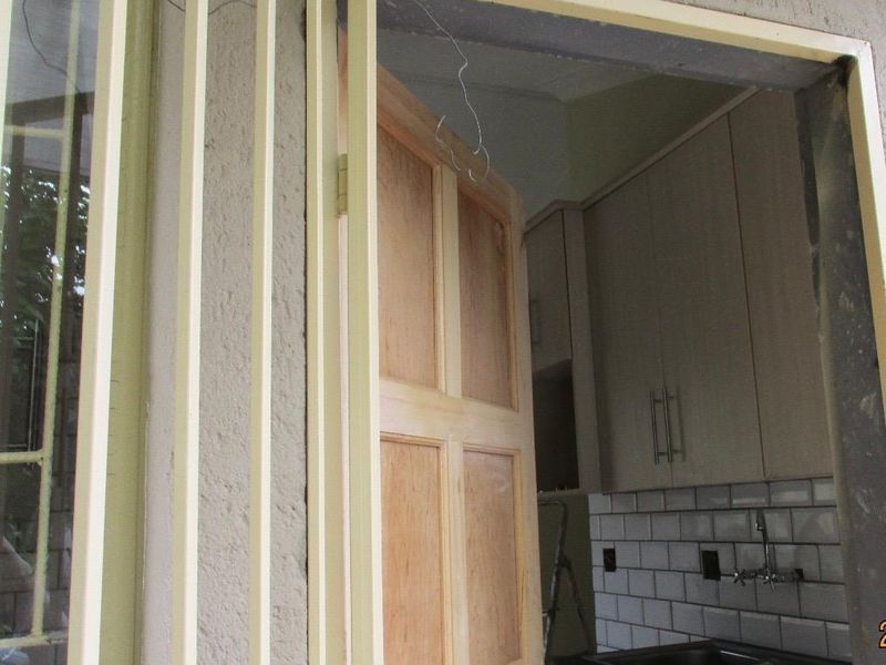 A compact kitchen featuring built-in cabinetry, a subway tile backsplash, and a stainless steel double sink, viewed through an open wooden door.