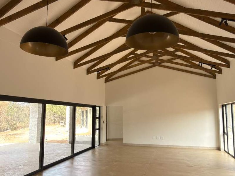 Spacious living area featuring a high vaulted ceiling with exposed timber trusses, polished concrete floors, and large sliding doors opening to the exterior.