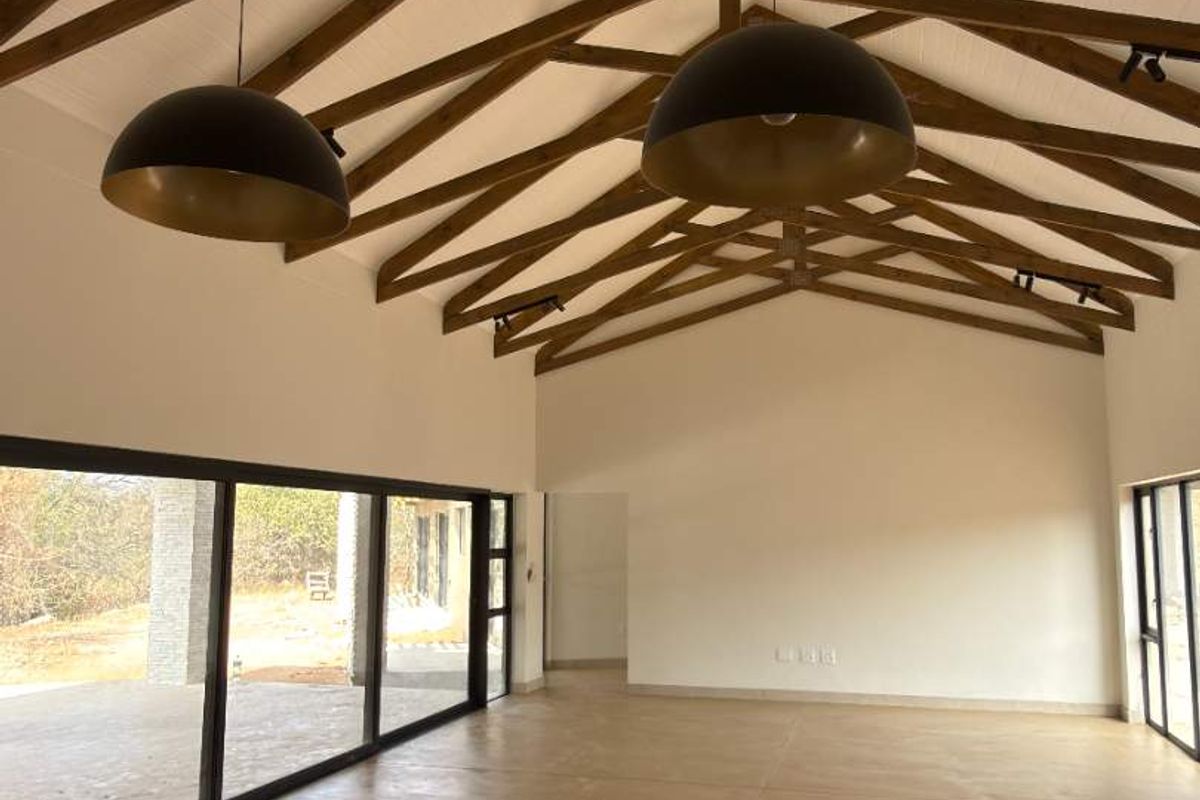 Spacious living area featuring a high vaulted ceiling with exposed timber trusses, polished concrete floors, and large sliding doors opening to the exterior.