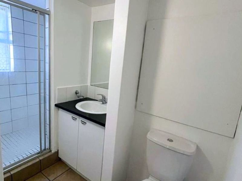 A functional bathroom featuring a shower enclosure, a vanity with a basin, and a standard toilet, finished with tiled flooring.