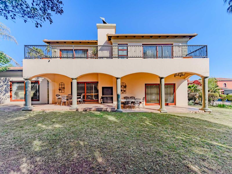 Rear view of the house featuring a spacious covered patio with a built-in braai, leading to an upper-level balcony with wrought iron railings.
