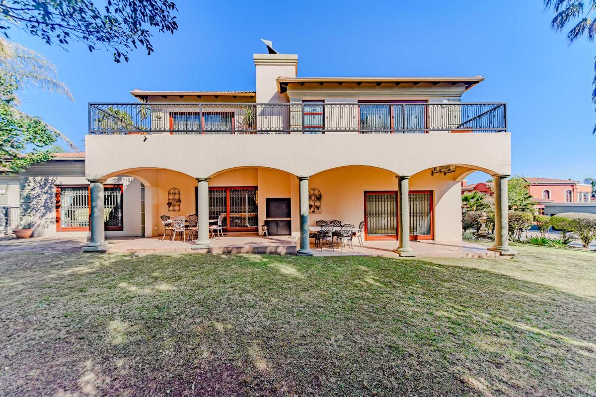 Rear view of the house featuring a spacious covered patio with a built-in braai, leading to an upper-level balcony with wrought iron railings.