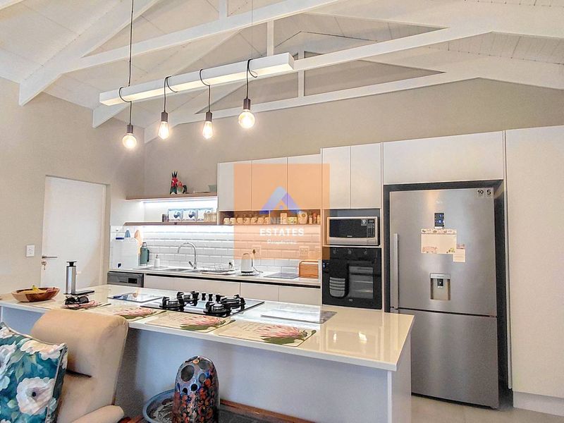 Modern kitchen featuring white cabinetry, stone countertops, subway tile backsplash, gas hob, built-in oven, and high vaulted ceilings with exposed rafters.