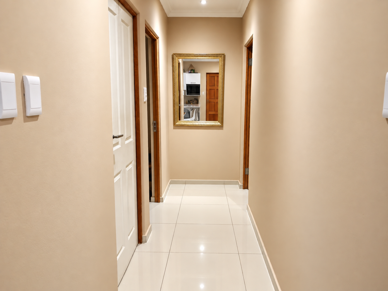 A clean, well-maintained hallway featuring neutral wall tones, polished floor tiles, and recessed downlighting, providing access to multiple rooms.