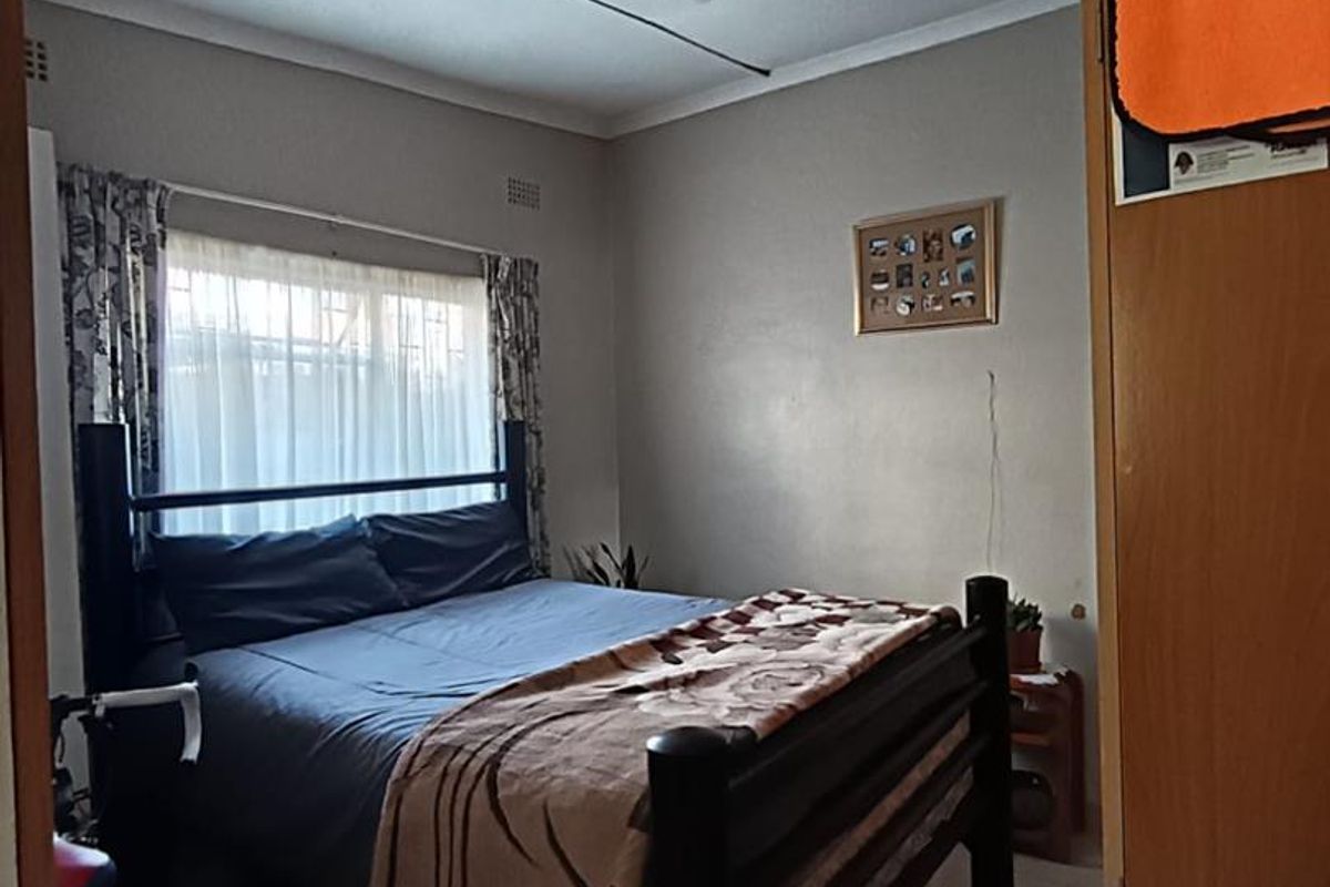 A functional bedroom featuring tiled flooring and a window with curtain tracks, providing a simple and practical living space.