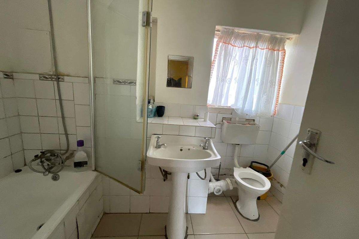 A dated bathroom featuring a pedestal basin, toilet, and a shower-over-bath combination with tiled finishes.